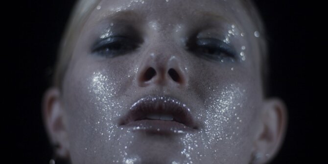 Extreme close-up of a face covered in silver glitter, eyes half closed – Ginette NY Ajna