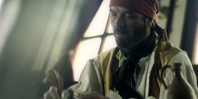 Pirate in a red bandana at a table in a ship's cabin lit by window light – La Buse docu-fiction