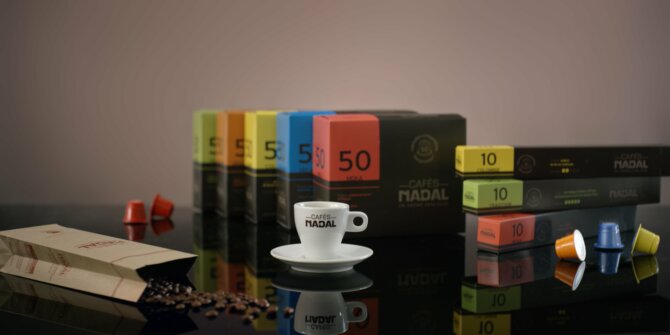 Cafés Nadal capsules, boxes and an espresso cup on a glossy black surface – packshot