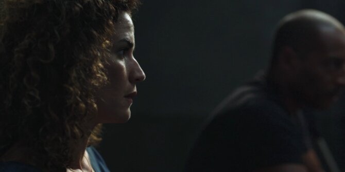 Curly-haired woman in profile facing a man in low light – OPJ Season 4 Bianca