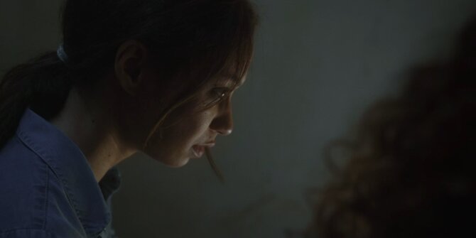 Young woman looking down, face half lit in a dark room – OPJ Season 4 Bianca
