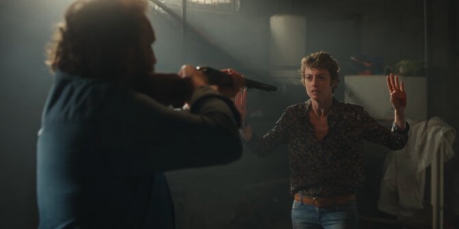 Man aiming a rifle at a woman raising her hand in a dusty shed – OPJ Season 6 Forbidden Fruit