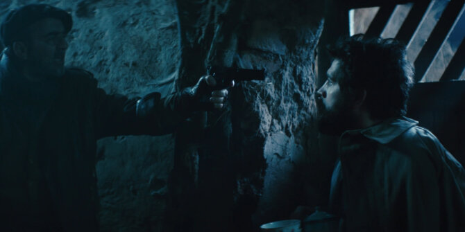 Man held at gunpoint against a stone wall in a dark cellar – Rhinozeros feature film